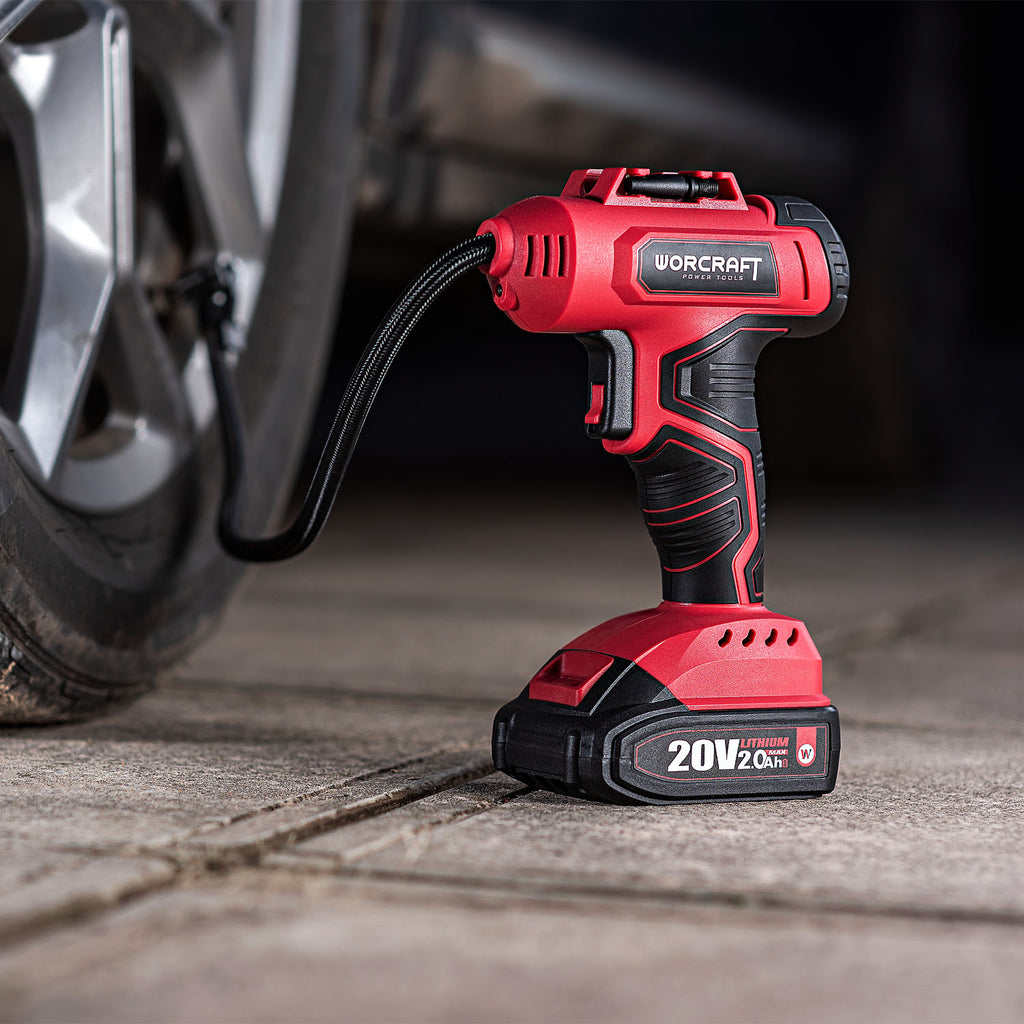 A red and black Worcraft cordless air compressor is shown plugged into a car tire valve on a concrete surface, with the brand name clearly visible on the handle and battery.