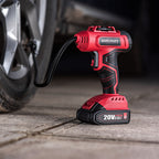 A red and black Worcraft cordless air compressor is shown plugged into a car tire valve on a concrete surface, with the brand name clearly visible on the handle and battery.