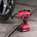 A red and black cordless air compressor tool with a flexible black hose, standing on a concrete surface next to a car tire. The brand name 'WORCRAFT' is visible on the side of the tool, and '20V 2.
