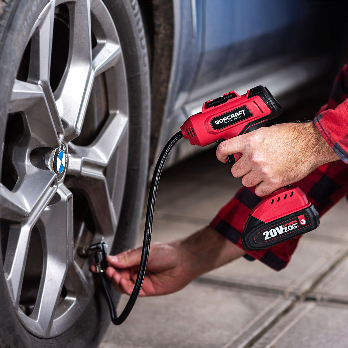 A person using a red and black cordless Worcraft 20V20C tire inflator on a silver car wheel