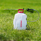 A white Worcraft backpack sprayer with a red cap and a long metal spray wand, set on a green grass lawn.