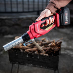 A person's hand holds a red and black Worcraft cordless firestarter over a pile of firewood logs, with a metal mouthpiece extended. The background is a dark, rustic outdoor setting.