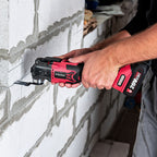 A person using a red and black Worcraft 20V MAX cordless oscillating multi-tool on a white brick wall in an outdoor or construction setting.