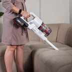 A person using a cordless Worcraft vacuum stick to clean couch cushions