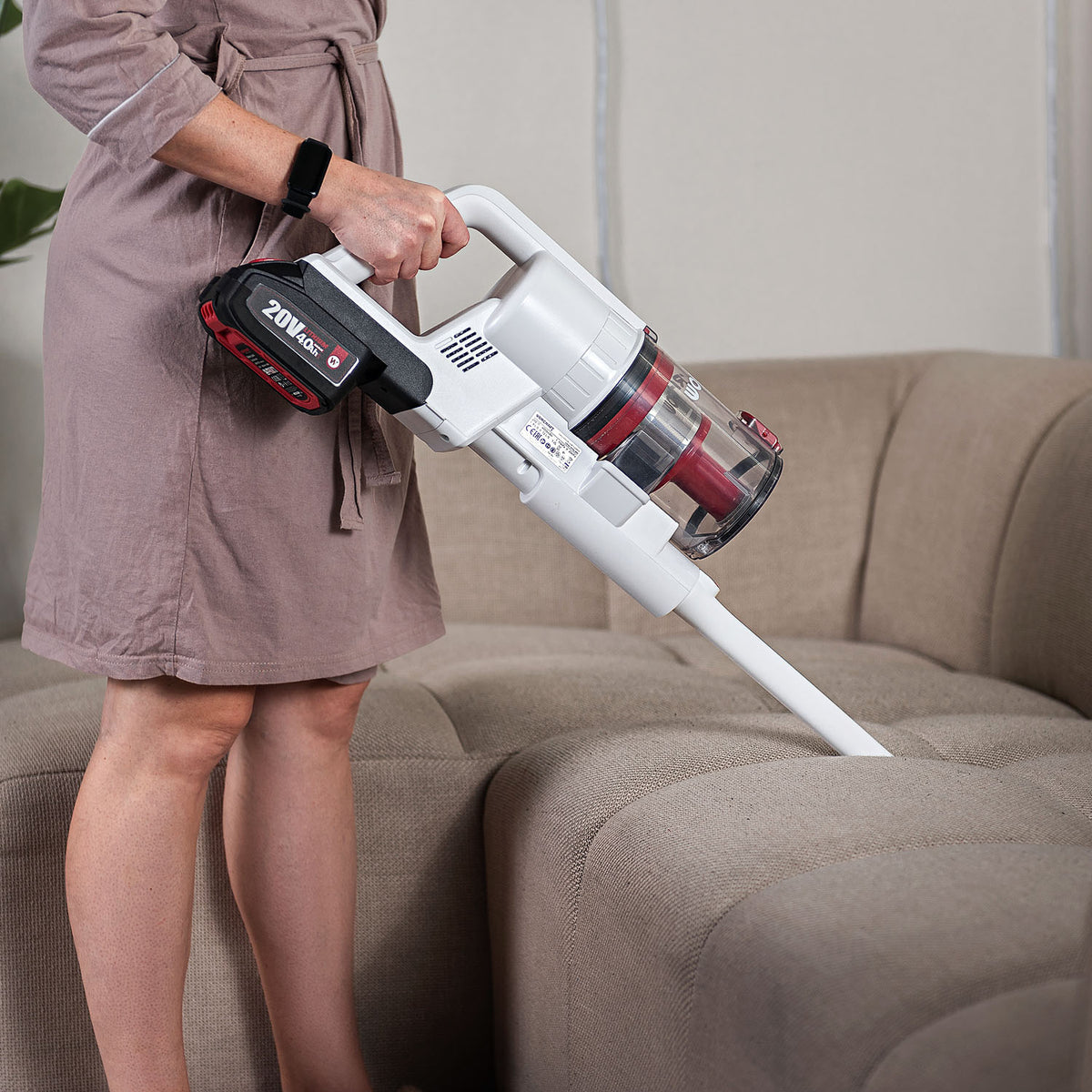 A person using a cordless Worcraft vacuum stick to clean couch cushions