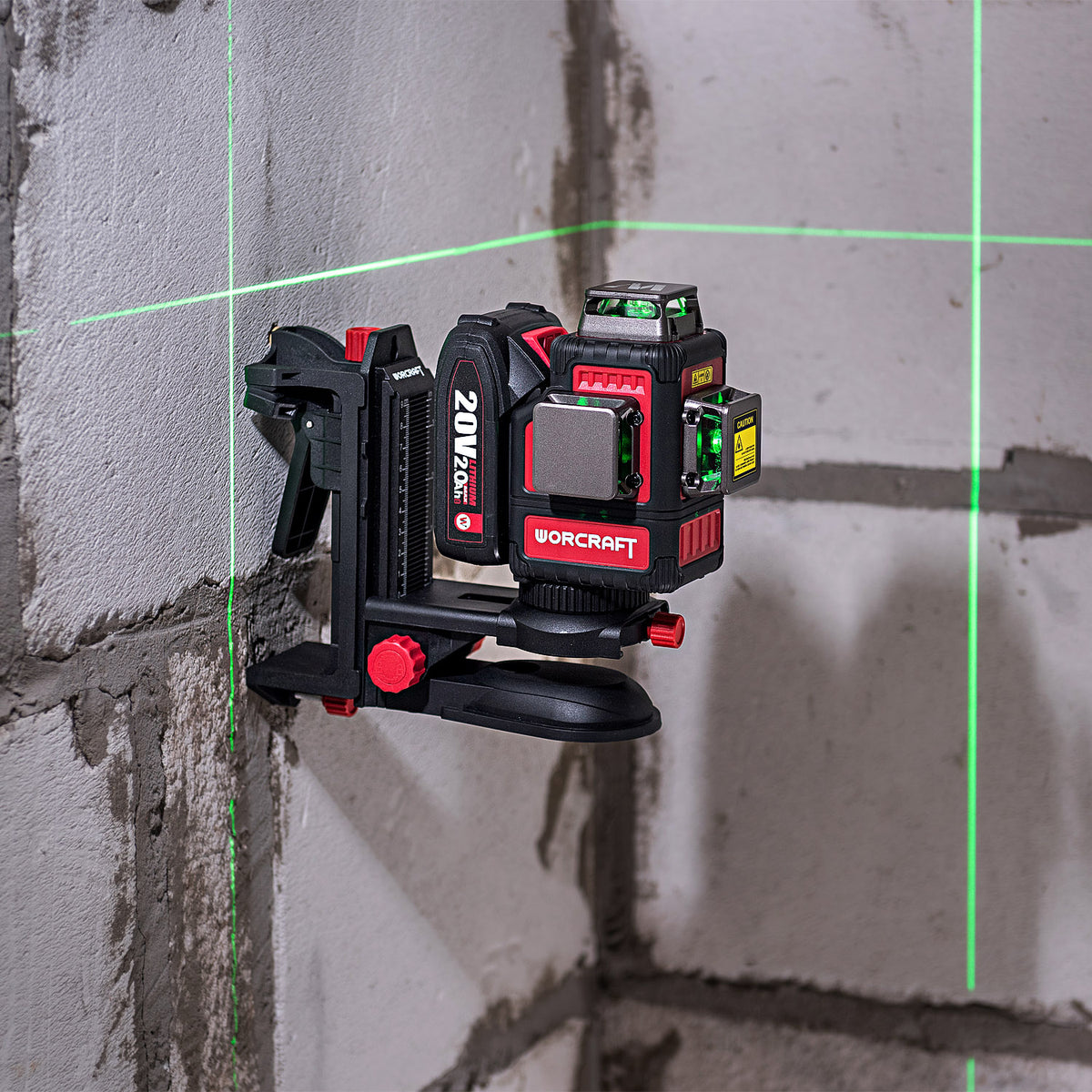 A red and black WorCraft 20V MAX laser level mounted on a gray concrete block wall, casting green laser lines across the wall.