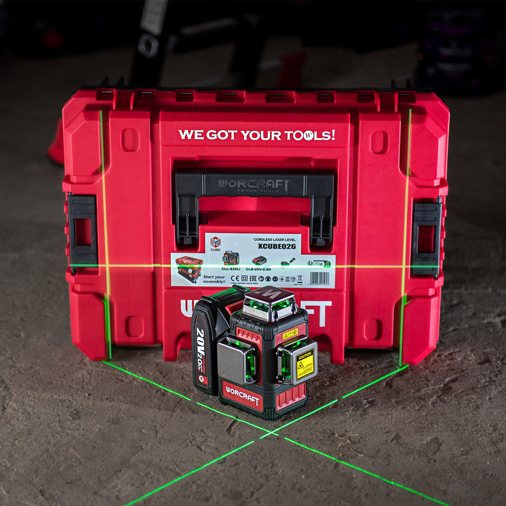 A red Worcraft Workstation carrying case with a black and red Worcraft XCUBE026 K20 Pro laser level placed in front of it on a concrete floor. Green and red laser lines are visible on the floor, and the background is a dark workshop environment.