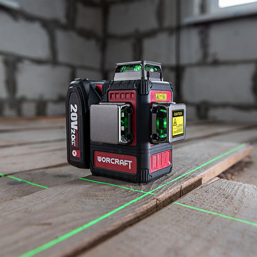 A WORCRAFT 20V 4S laser level standing on wooden planks in a construction setting, with green laser lines projected on the floor and a blurred brick wall in the background.