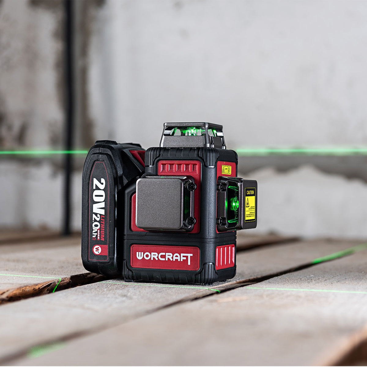 A WORCRAFT 20V 2.0Ah laser level standing on a concrete floor, with its green laser lines projected across the background.