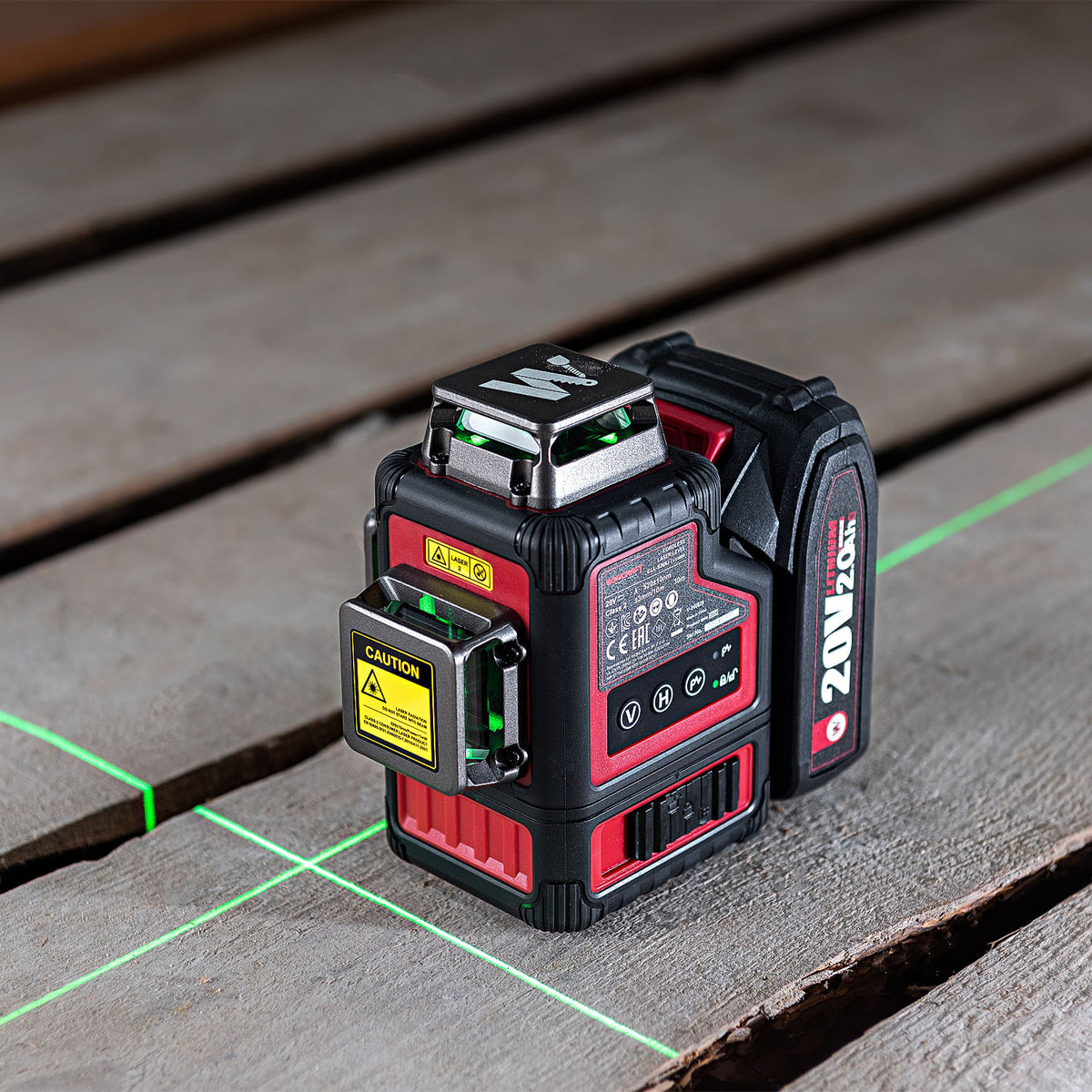 A red and black 20V 1M laser level sits on a weathered wooden deck, emitting a green laser grid across the surface.