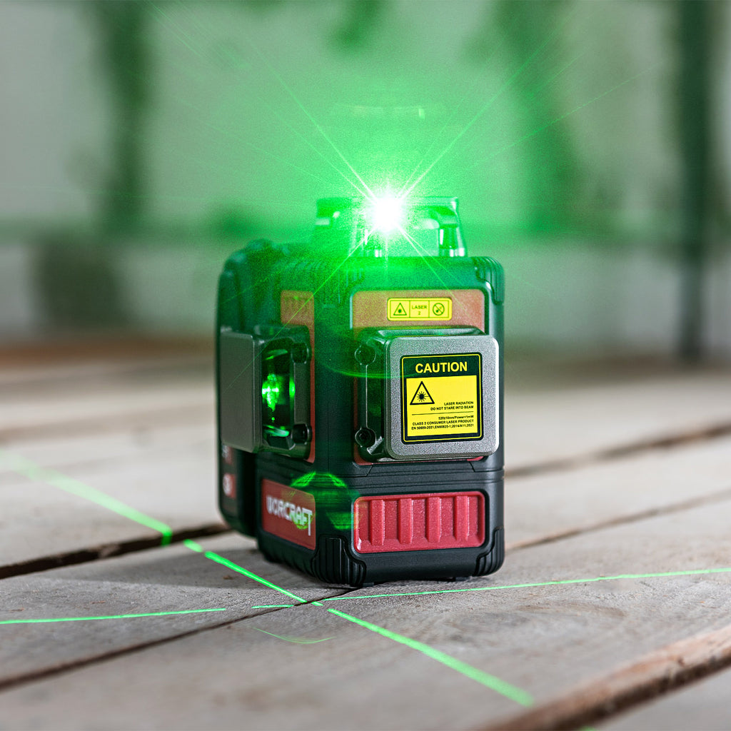 A Worcraft brand green laser level device on a wooden deck, emitting a bright green laser beam upward and crosswise across the surface.