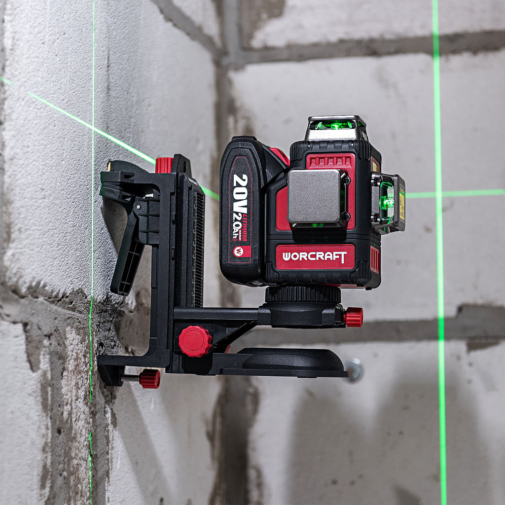A red and black WORCRAFT 20V MAX 3-in-1 laser level mounted on a black clamp against an unfinished concrete wall, with green laser lines projected on the wall.